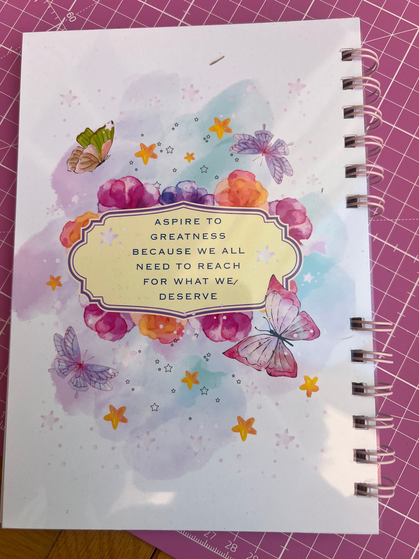Notebook with butterfly design and motivational quote on a pink cutting mat.