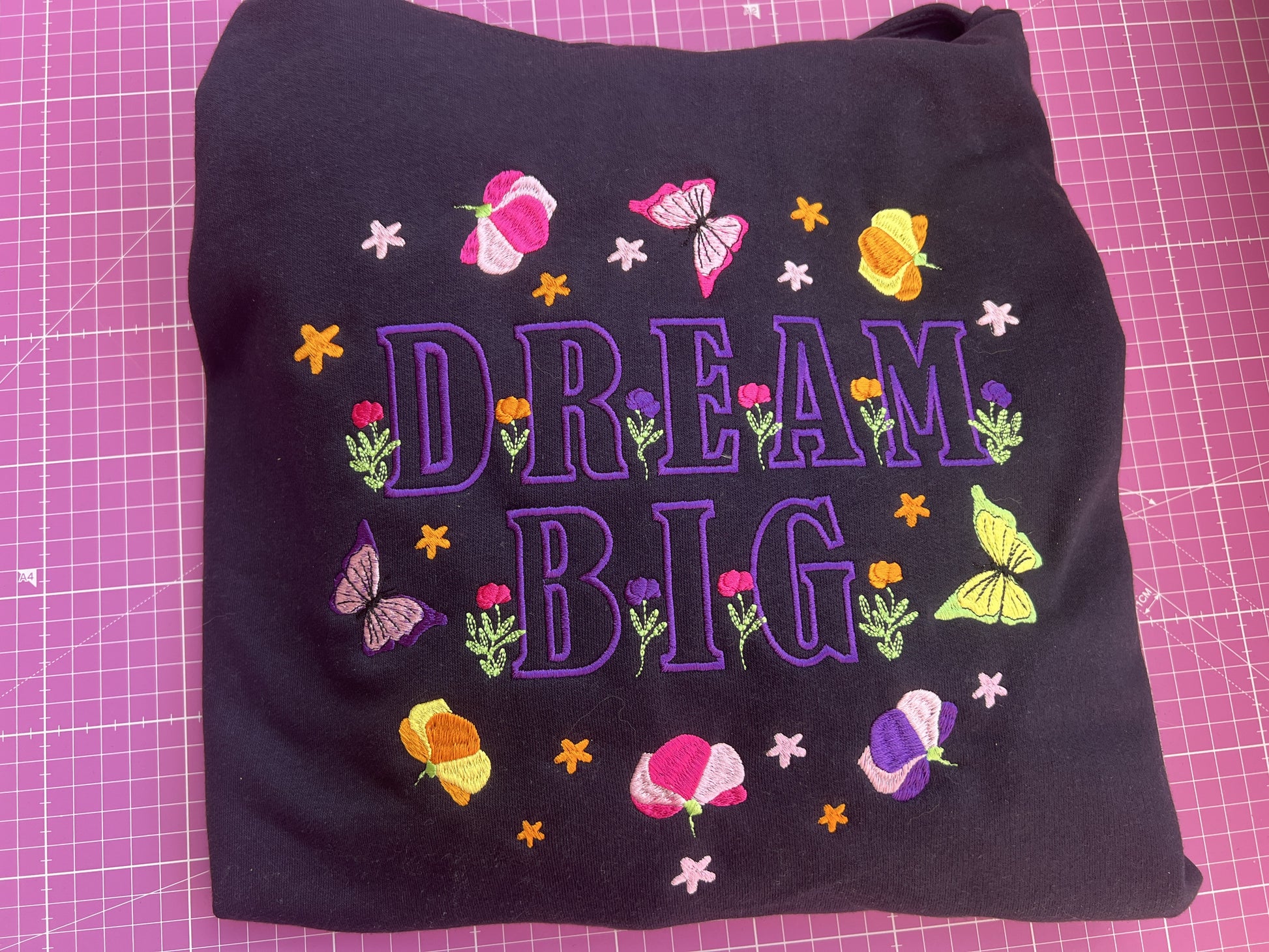 Black fabric with 'Dream Big' text and colorful flowers on a pink grid background