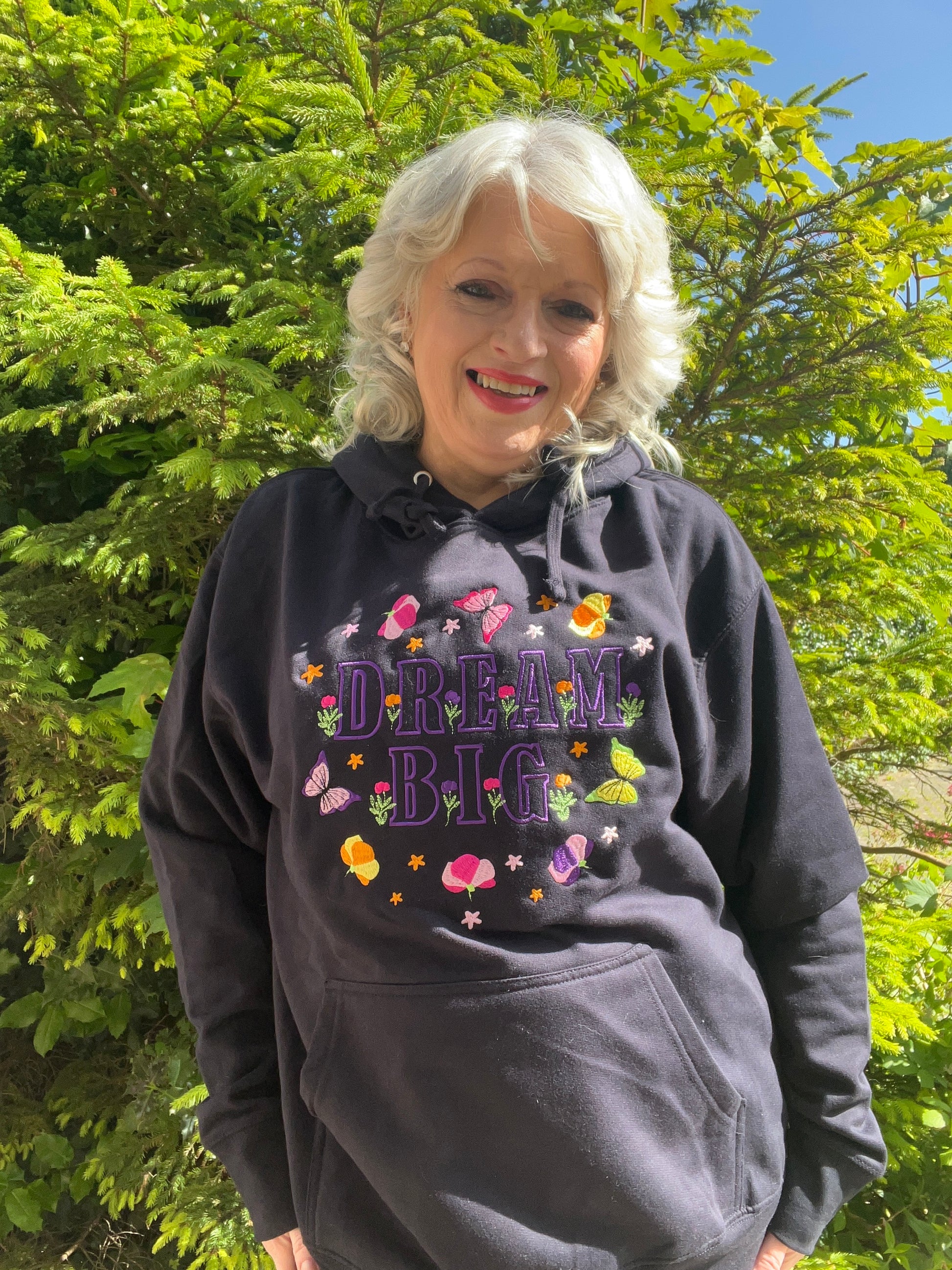 Woman wearing a black hoodie with 'Dream Big' text and colorful graphics outdoors.