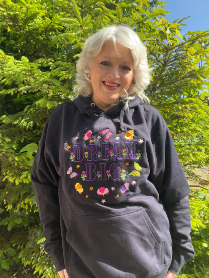Woman wearing a black hoodie with 'Dream Big' text and colorful graphics outdoors.
