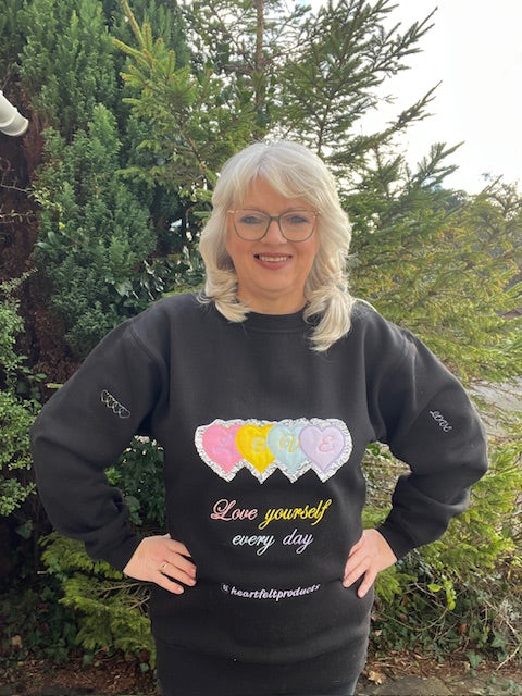 Person wearing a black sweatshirt with colorful heart design and text outdoors.
