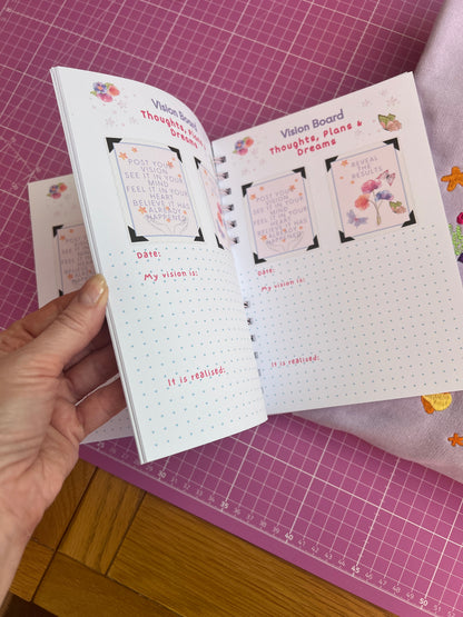 Hand holding a small book with decorative pages on a pink cutting mat.