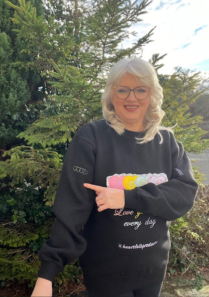 Person wearing a black sweatshirt with colorful text and graphics outdoors.